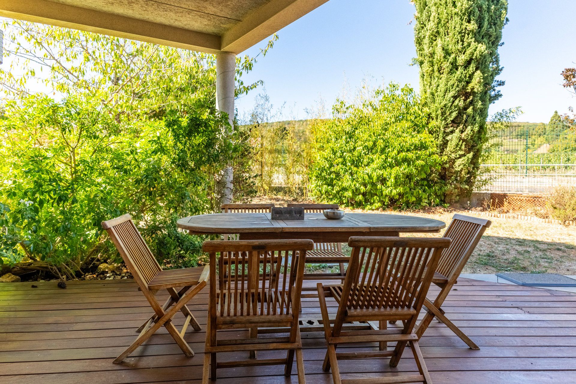 Una terraza exterior de madera con una mesa redonda y cuatro sillas.