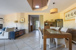 A modern living room with a dining area, featuring a sofa, a coffee table, a dining table with chairs, a cabinet, and a television. - Le Clos de Marsannay –4-Bedroom House (Marsannay-la-Côte)