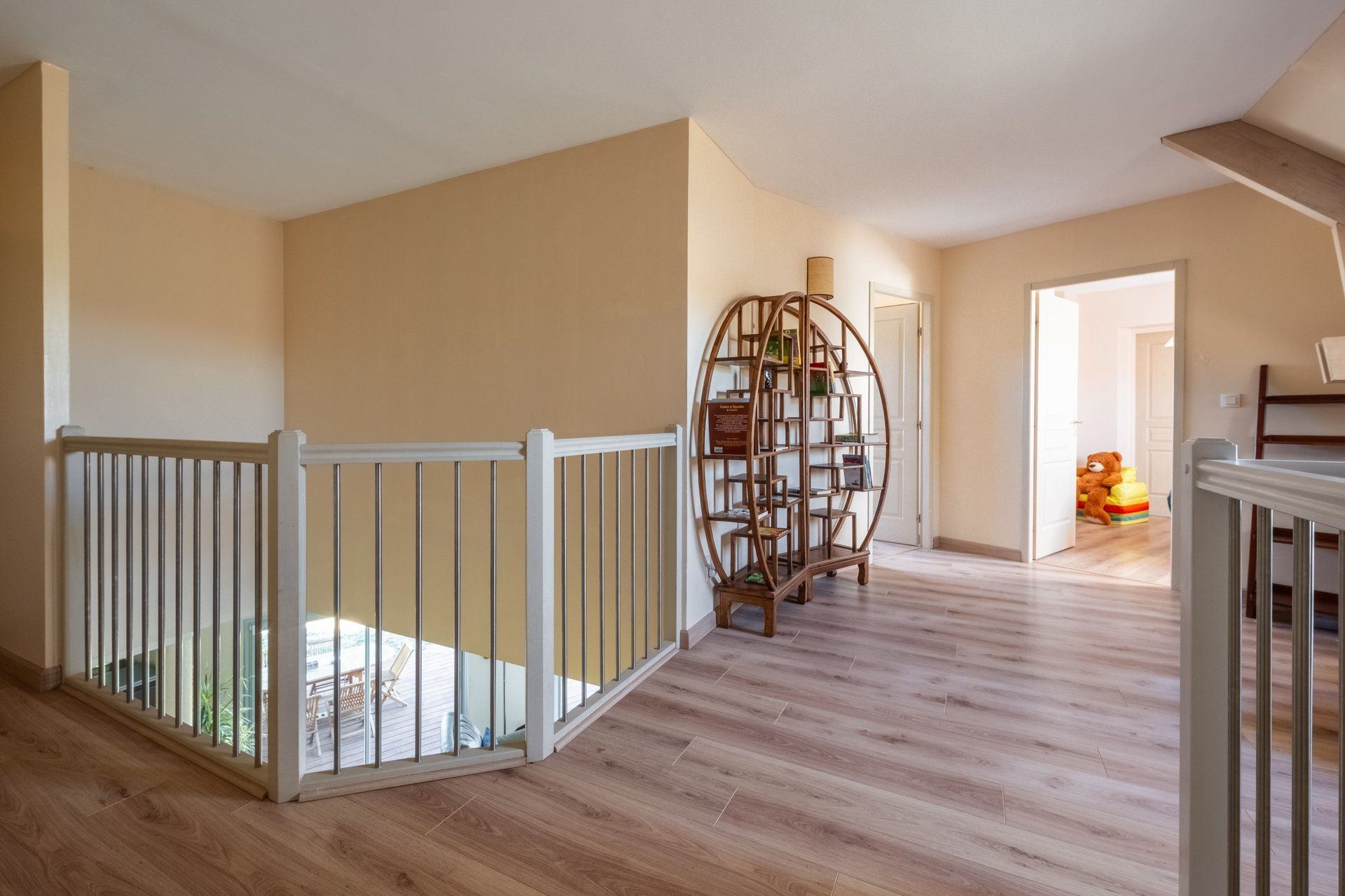 Un pasillo amplio con suelo de madera, baranda blanca y un estante de madera decorativo con libros.