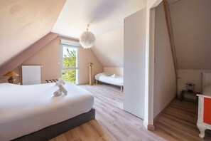 Une chambre avec un plafond en pente, un lit, une table de chevet, une lampe et une fenêtre donnant sur un paysage verdoyant.