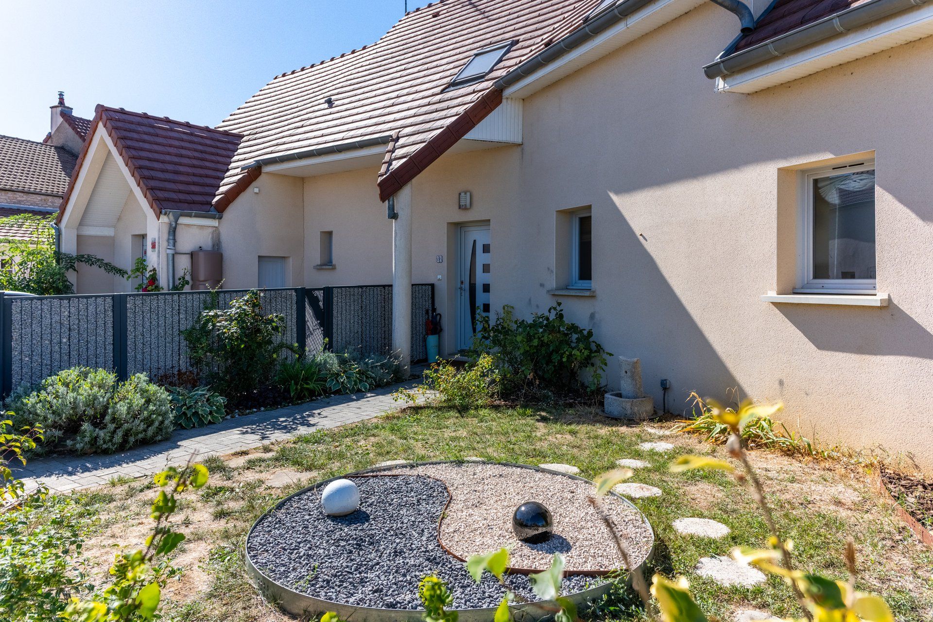 A residential property with a paved driveway, a circular garden with a central stone feature, and a house with a tiled roof and a white door.