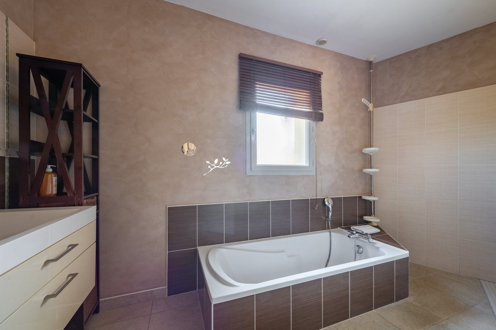 A modern bathroom with a bathtub, a window with blinds, and a wooden cabinet.
