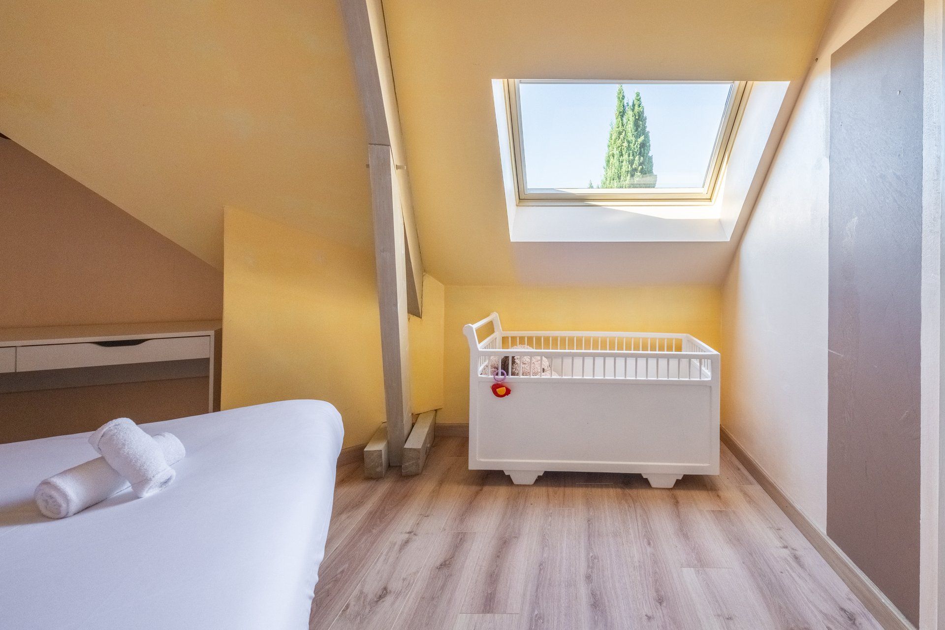 A room with a bed, a crib, a window, and a skylight.