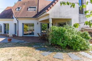 Une maison avec un patio, un espace extérieur aménagé et abrité, et un grand arbuste.