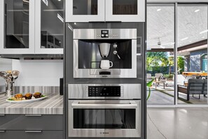Eine Küche mit einer Bosch-Kaffeemaschine, einem großen Backofen und einer Marmarbeilung mit Muffins.