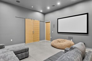 Ein moderner Heimkino-Raum mit grauen Wänden, einem großen Flachbildfernseher, einem Sitzsack und grauen Sofas.