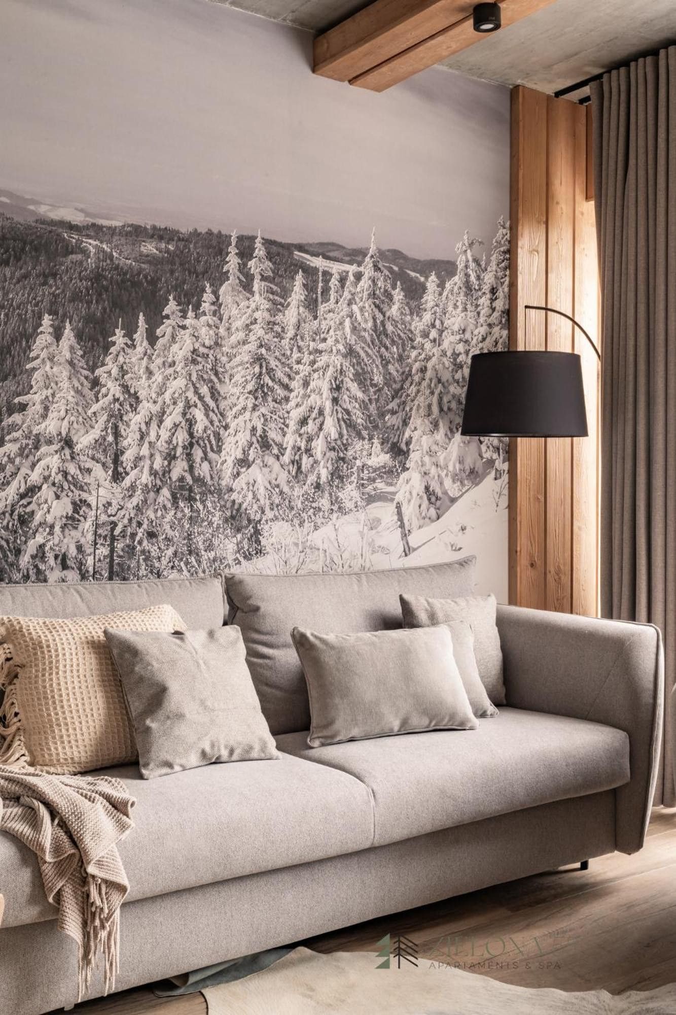 En moderne stue med sofa, lampe og et stort vægmaleri af en snefyldt skov.