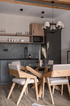 Une cuisine moderne avec des meubles en bois, un four à micro-ondes encastré et un coin repas comprenant une table en verre et des chaises en bois.