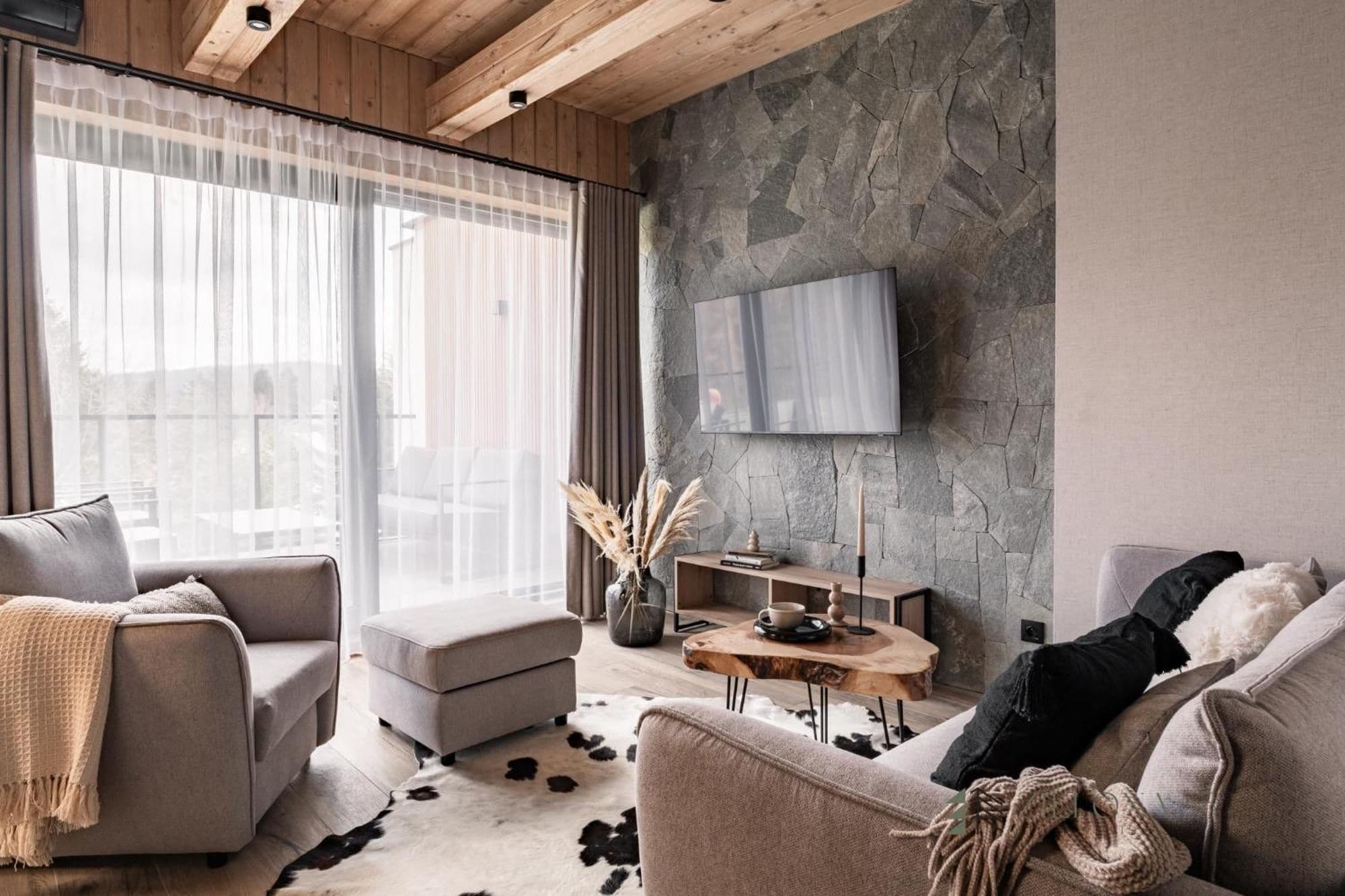 A modern living room with a stone wall, a flat-screen TV mounted above it, and a cozy seating area with a sofa and armchairs.