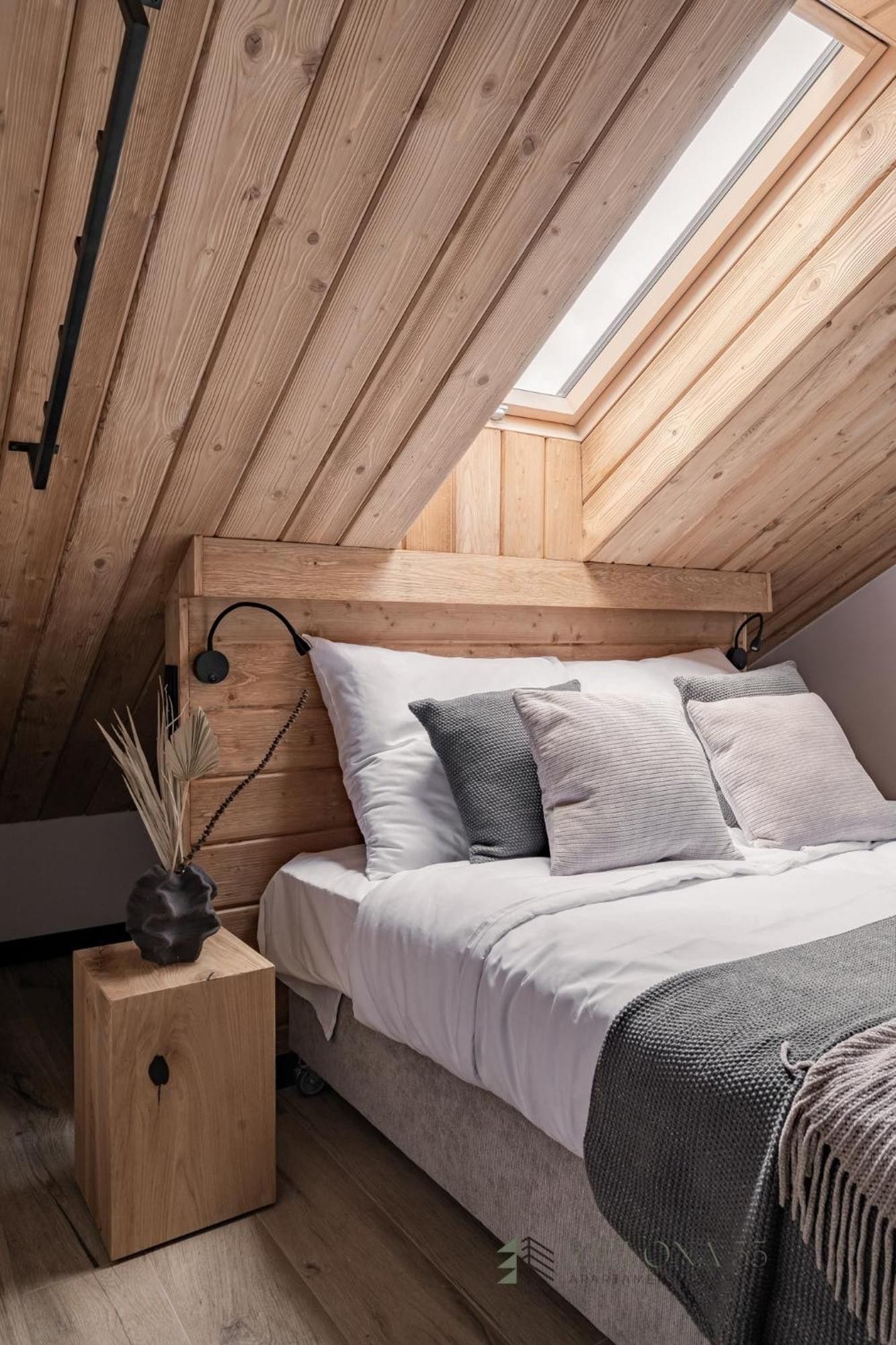 A bedroom with a sloped ceiling, wooden headboard, and a skylight.