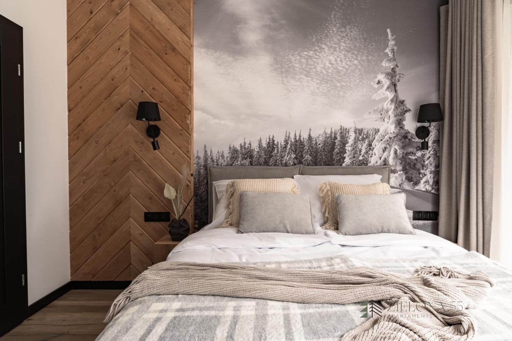 Une chambre avec un mur orné d’un motif en chevrons, un lit recouvert de nombreux coussins et une grande fresque murale représentant une forêt enneigée.