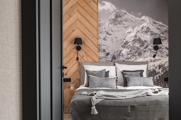 A bedroom with a bed, two bedside lamps, a nightstand, and a wall with a mountain image.