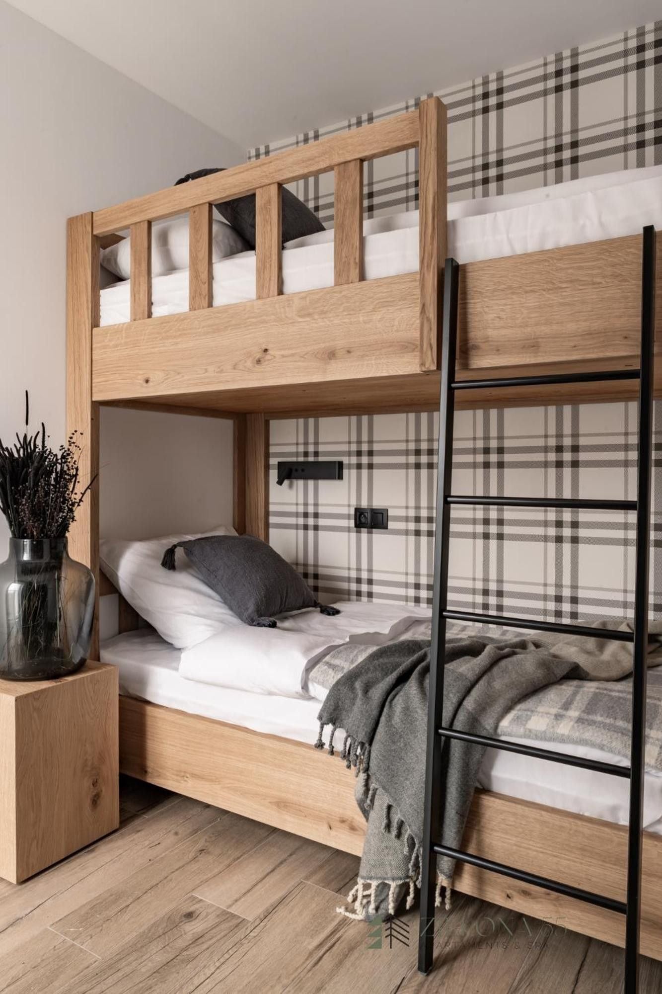 Ein Etagenbett mit Holzbettgestell, ein Nachttisch mit einer Vase und eine Wand mit Karomuster.