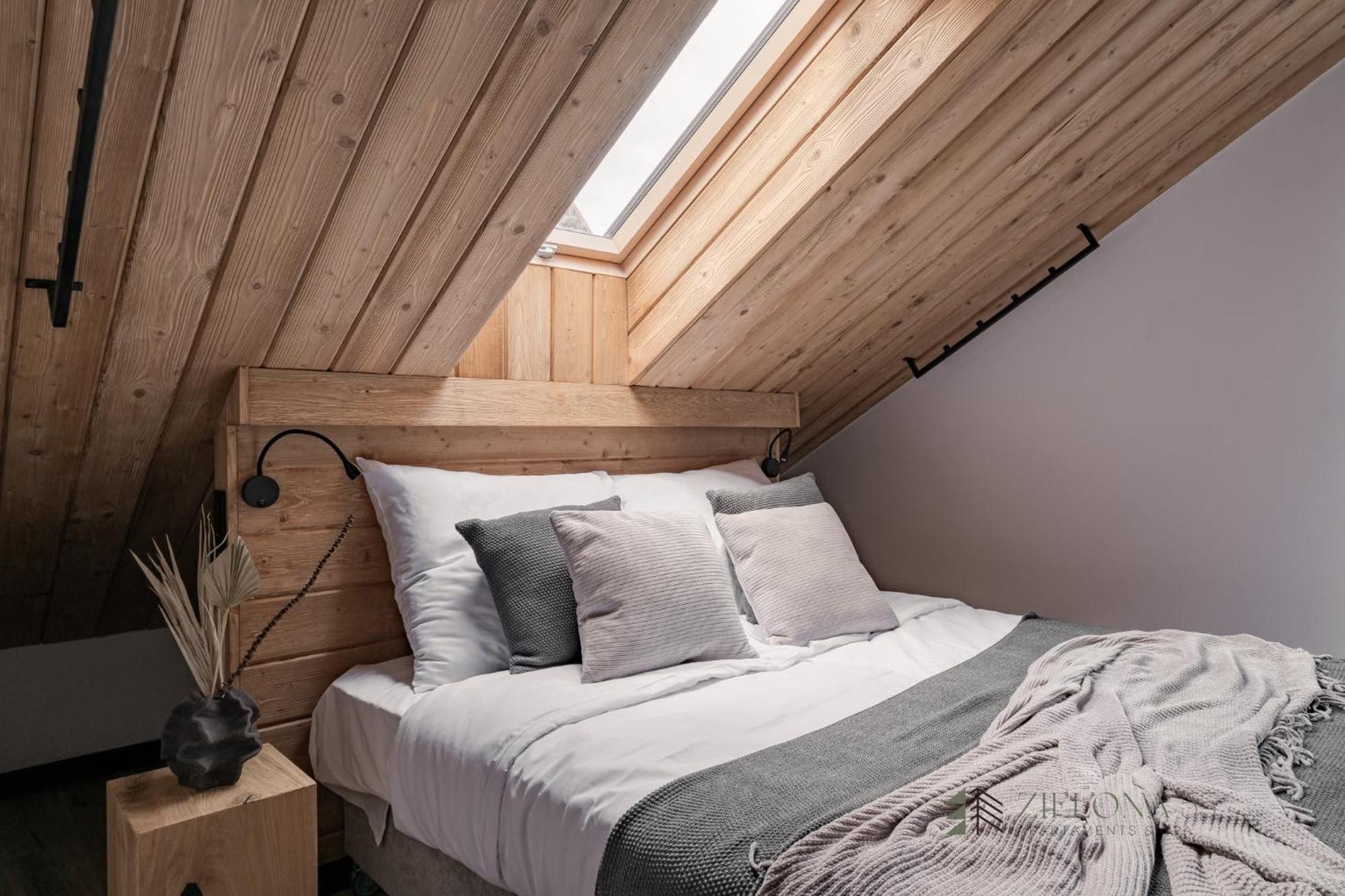 A bedroom with a sloped ceiling, wooden headboard, and a skylight.