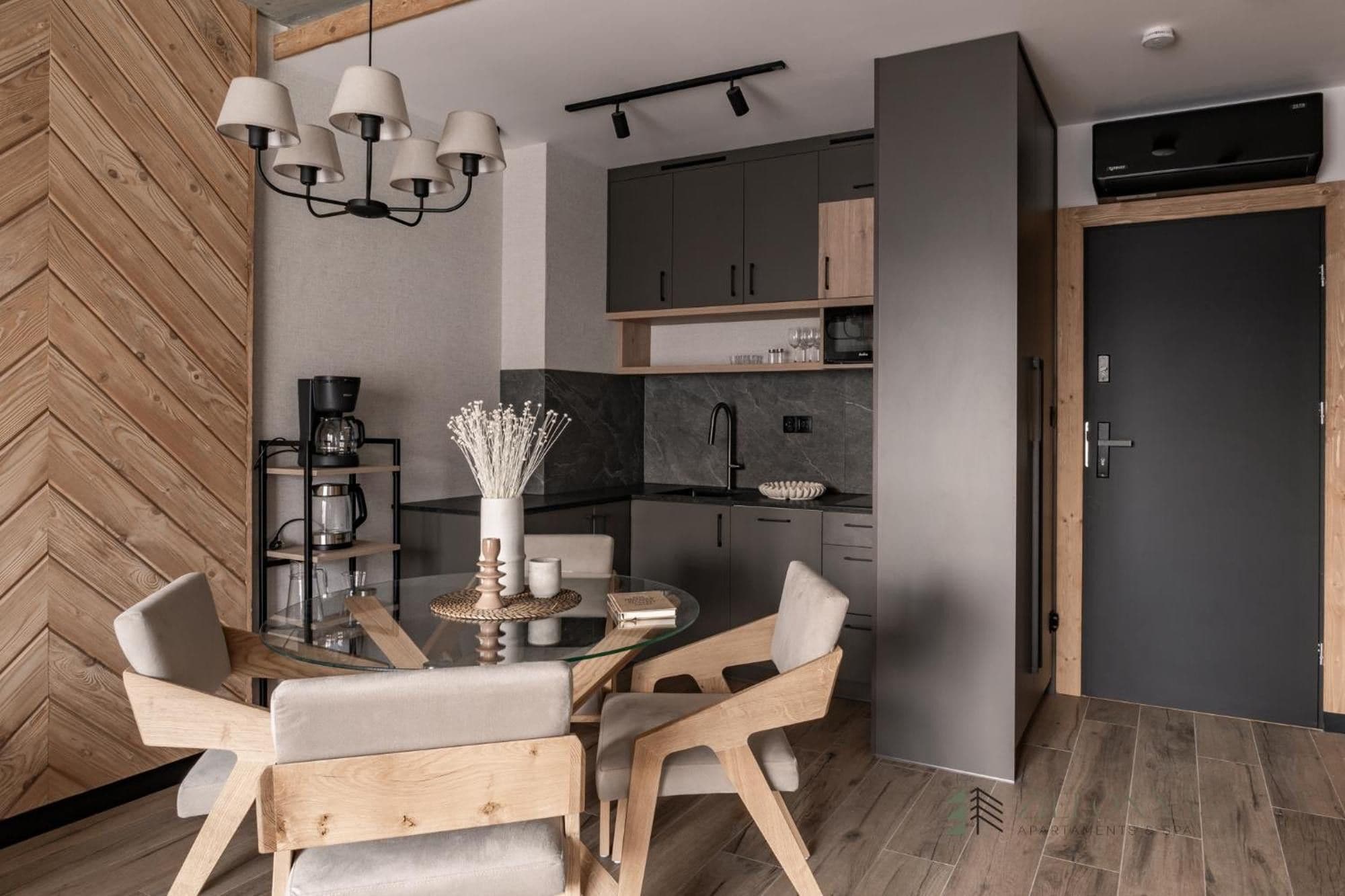 Een moderne keuken met een eethoek, met een wand van visgraatmotief hout, een centraal kookeiland met stoelen en een hanglamp.