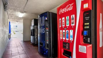 Un couloir où se trouvent des distributeurs automatiques, dont un distributeur de Coca-Cola et un autre avec un design bleu.
