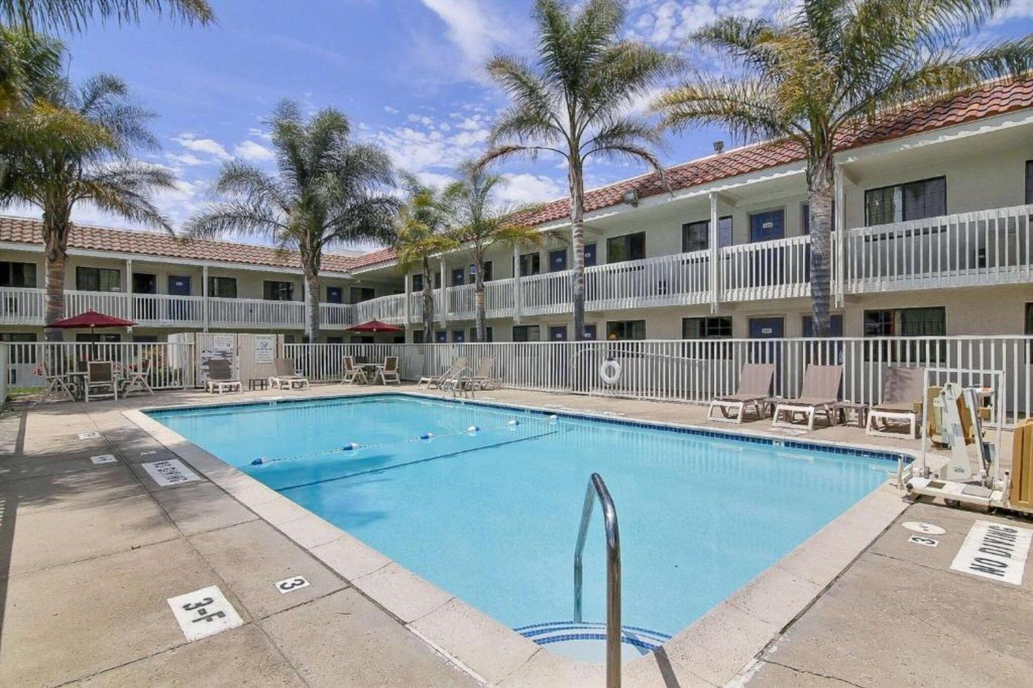 A hotel with a swimming pool, multiple balconies, and palm trees.