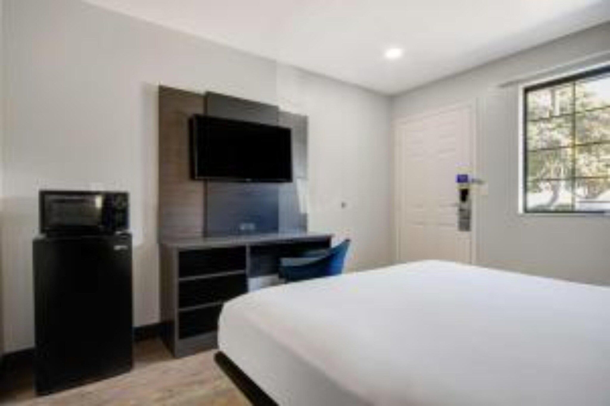 A hotel room with a bed, a desk with a computer, a television, and a window.