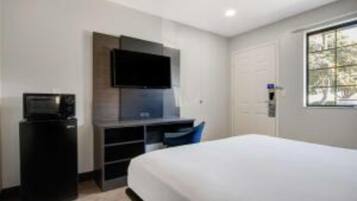 A hotel room with a bed, a desk with a computer, a television, and a window.
