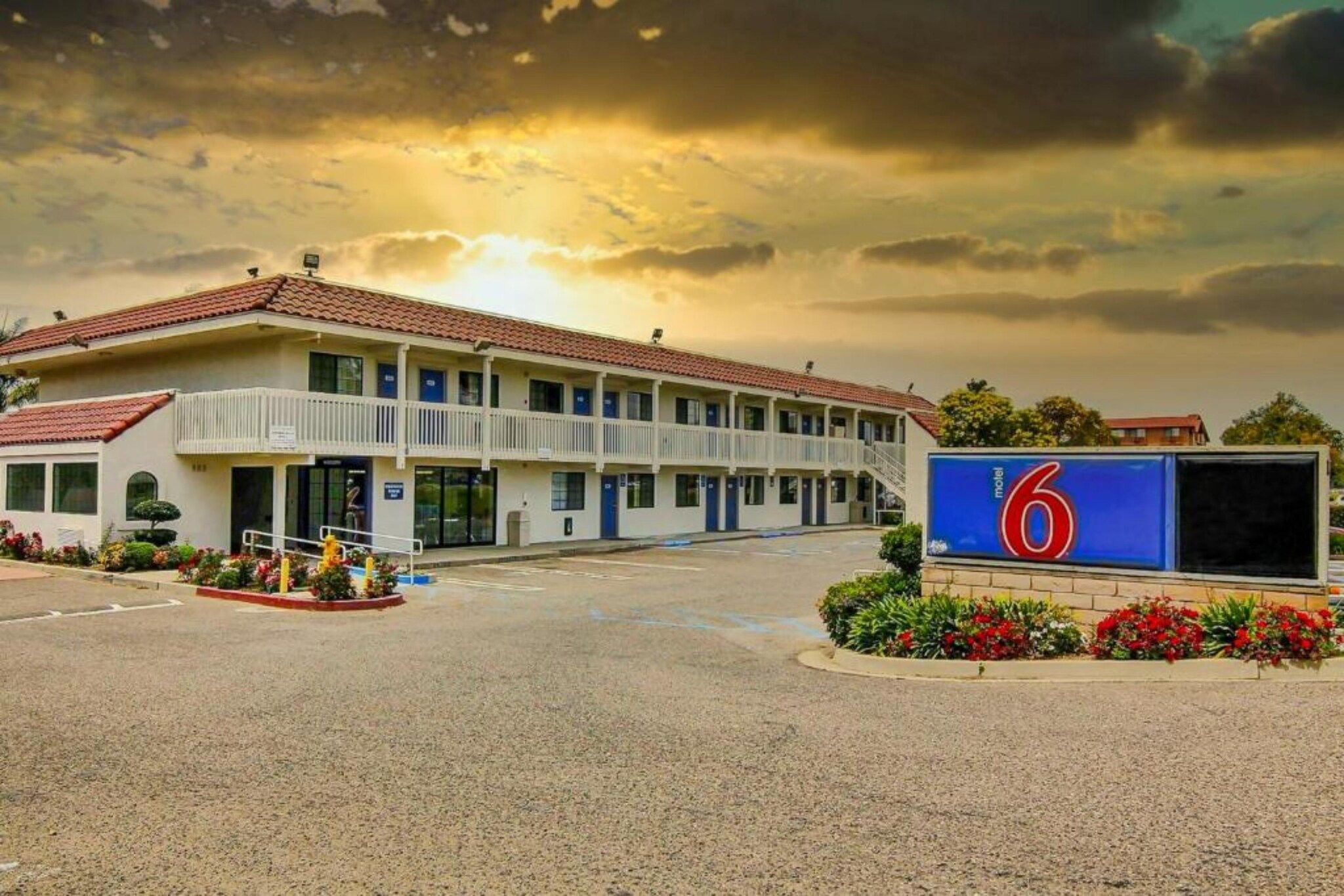 A motel with a two-story building, a parking lot, and a large sign with the number 6.