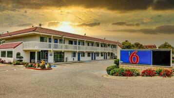 A motel with a two-story building, a parking lot, and a large sign with the number 6.