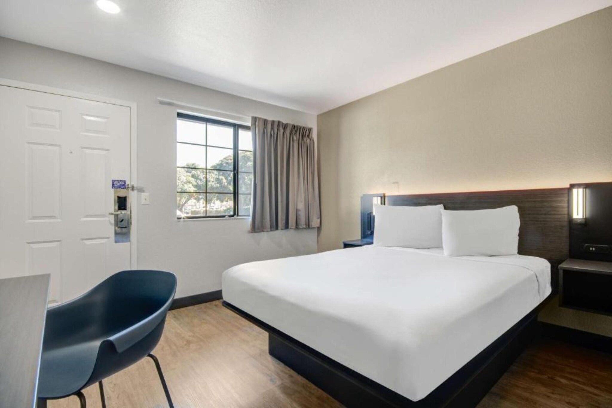 A hotel room with a bed, a desk, and a window with curtains.