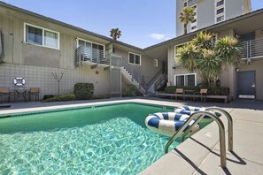 A swimming pool with a clear blue water surface, surrounded by a tiled deck area with outdoor seating and a staircase leading to an upper level. - The Blue Lagoon - in Pacific Beach w/ comm pool (San Diego)