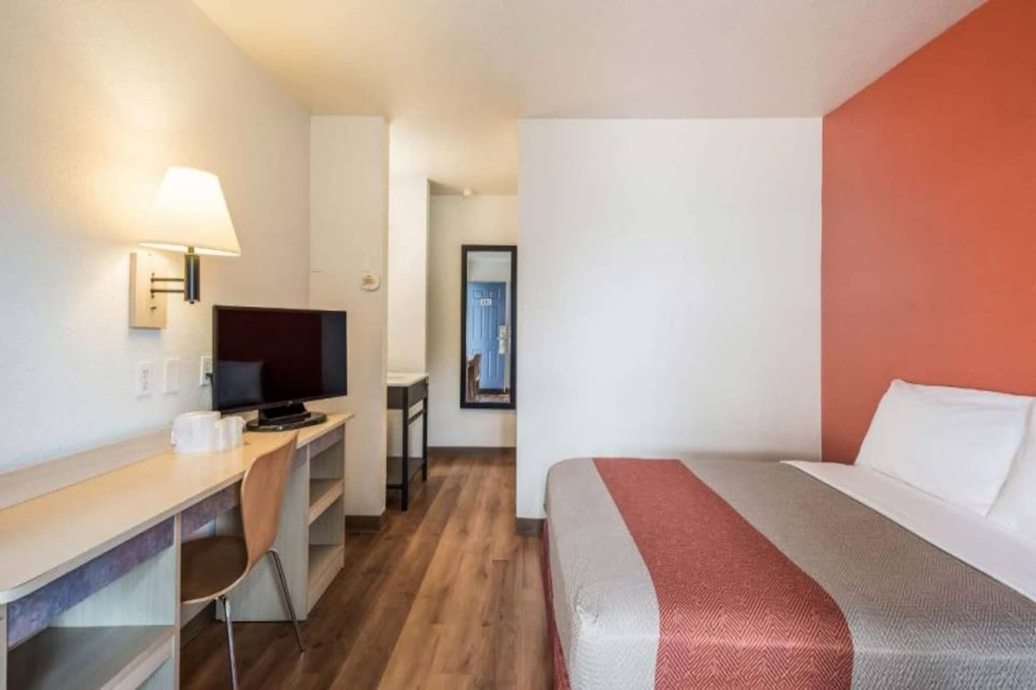 A hotel room with a bed, desk, chair, television, and a lamp.