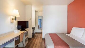 A hotel room with a bed, desk, chair, television, and a lamp.