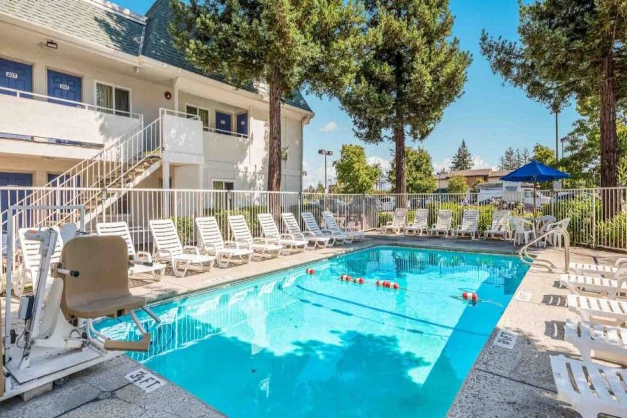 A swimming pool with lounge chairs and a building with blue doors in the background.