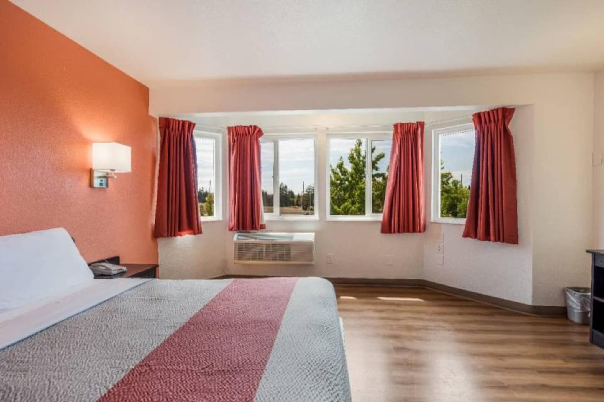 Una habitación de hotel con cama, ventana con cortinas, un calentador y vista a follaje exterior.