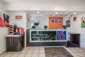 Una reception con una scrivania e un display digitale che mostra un messaggio, il logo numero 6 sul bancone e una parete decorata con diversi manifesti.