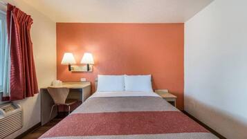 A hotel room with a bed, two bedside lamps, a desk with a chair, and a window with curtains.