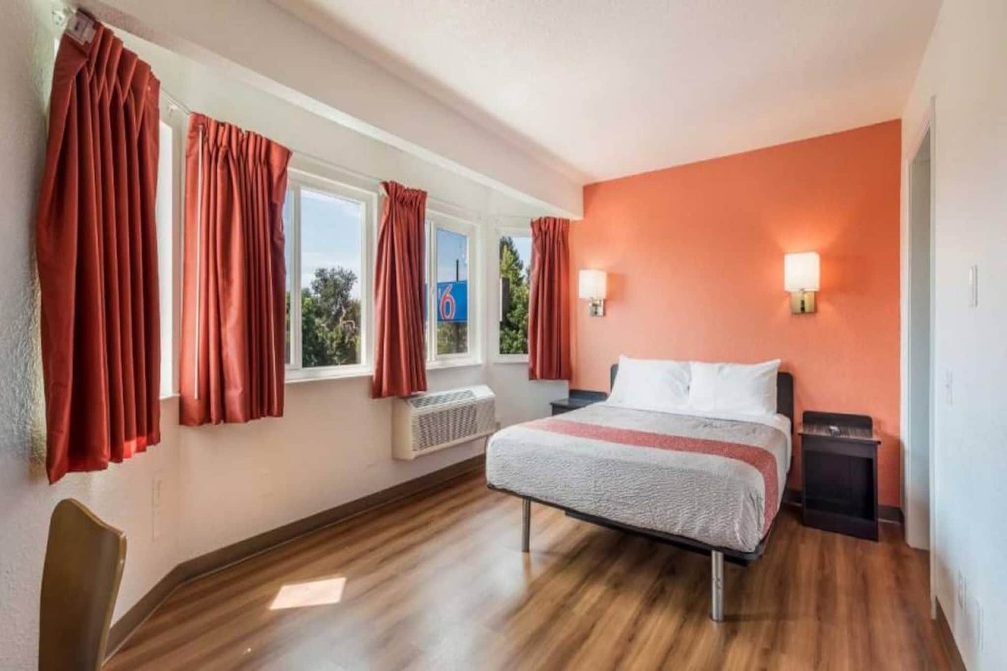 A bedroom with a bed, two bedside tables, a radiator, and curtains on windows.