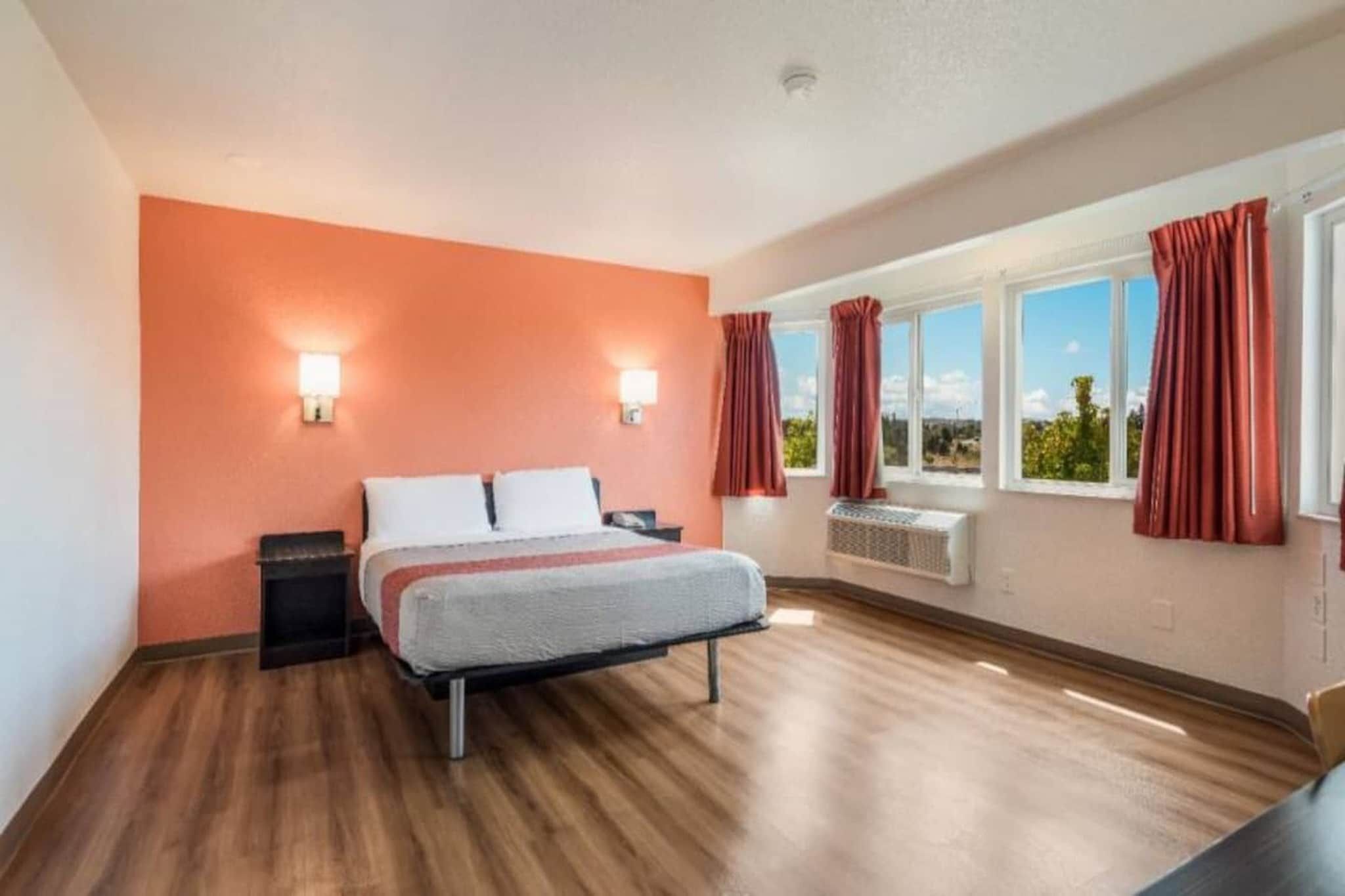 A hotel room with a bed, two wall-mounted lights, a window with curtains, and a view of the outdoors.
