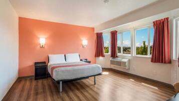 A hotel room with a bed, two wall-mounted lights, a window with curtains, and a view of the outdoors.