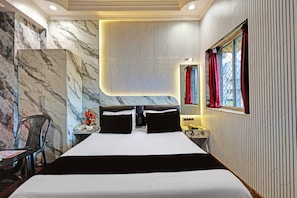 Una habitación de hotel con una cama grande, una silla, una mesita de noche con un teléfono y una ventana con cortinas.