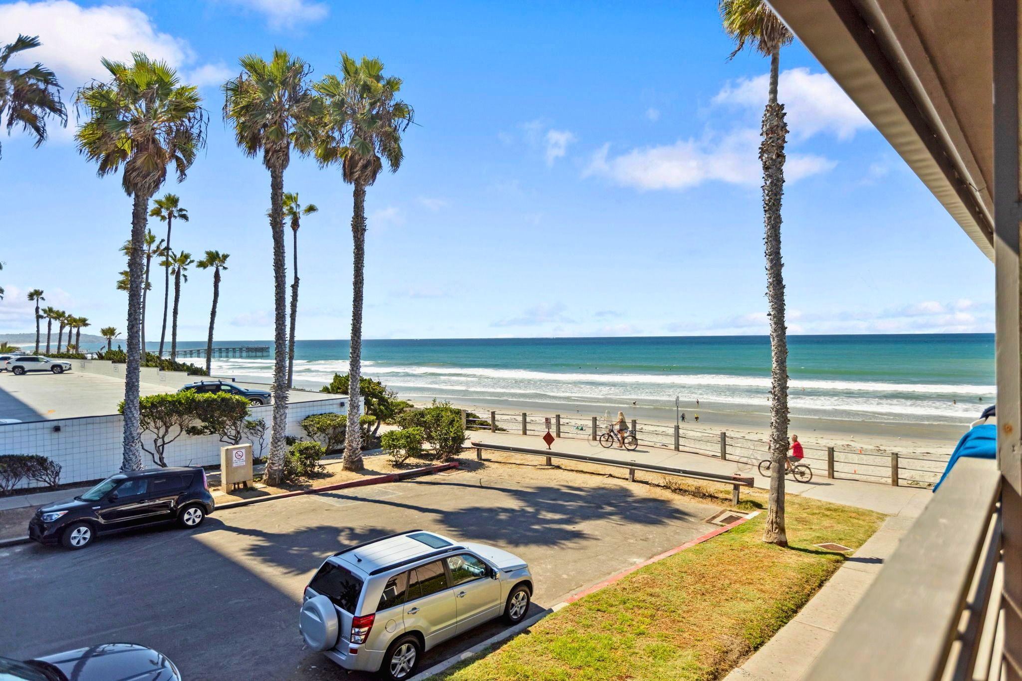 A coastal view with palm trees, a parking area, and a beach in the background.