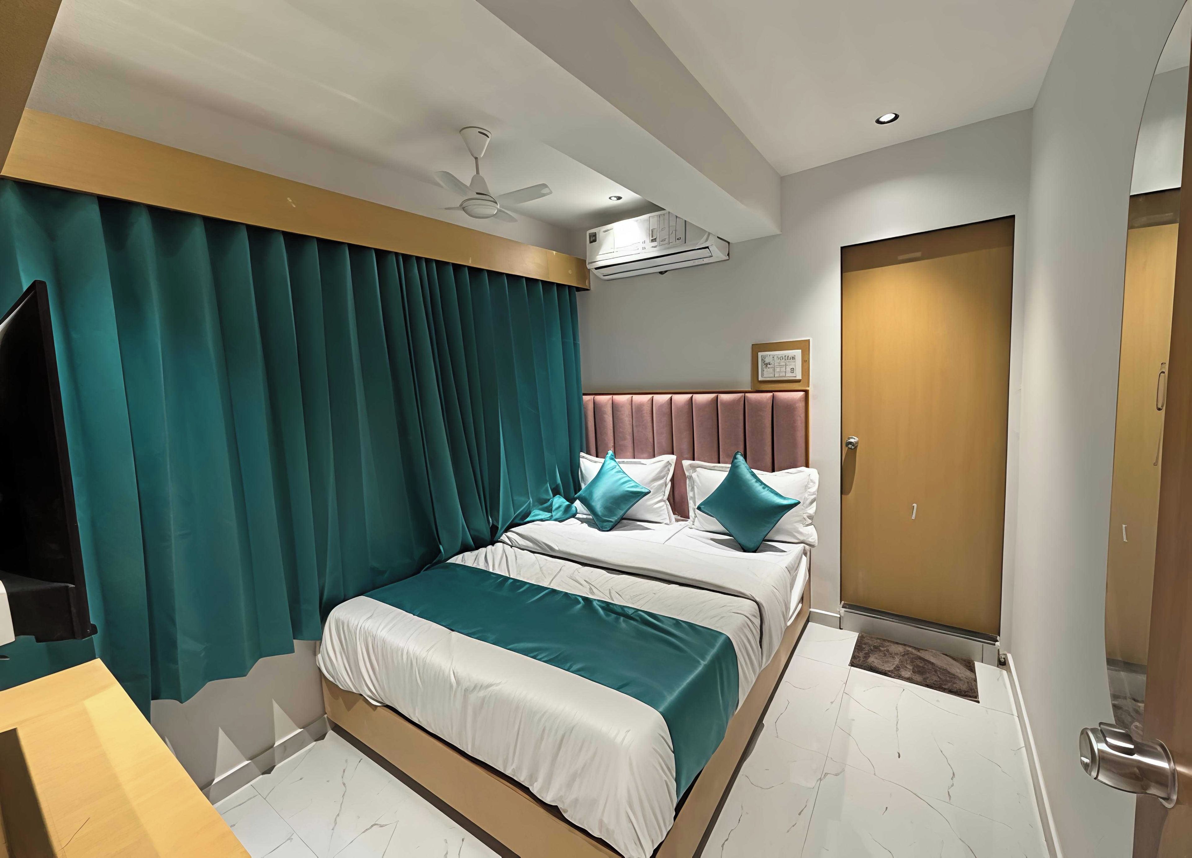 A hotel room with a bed, curtains, a ceiling fan, an air conditioning unit, a wooden door, and a marble floor.
