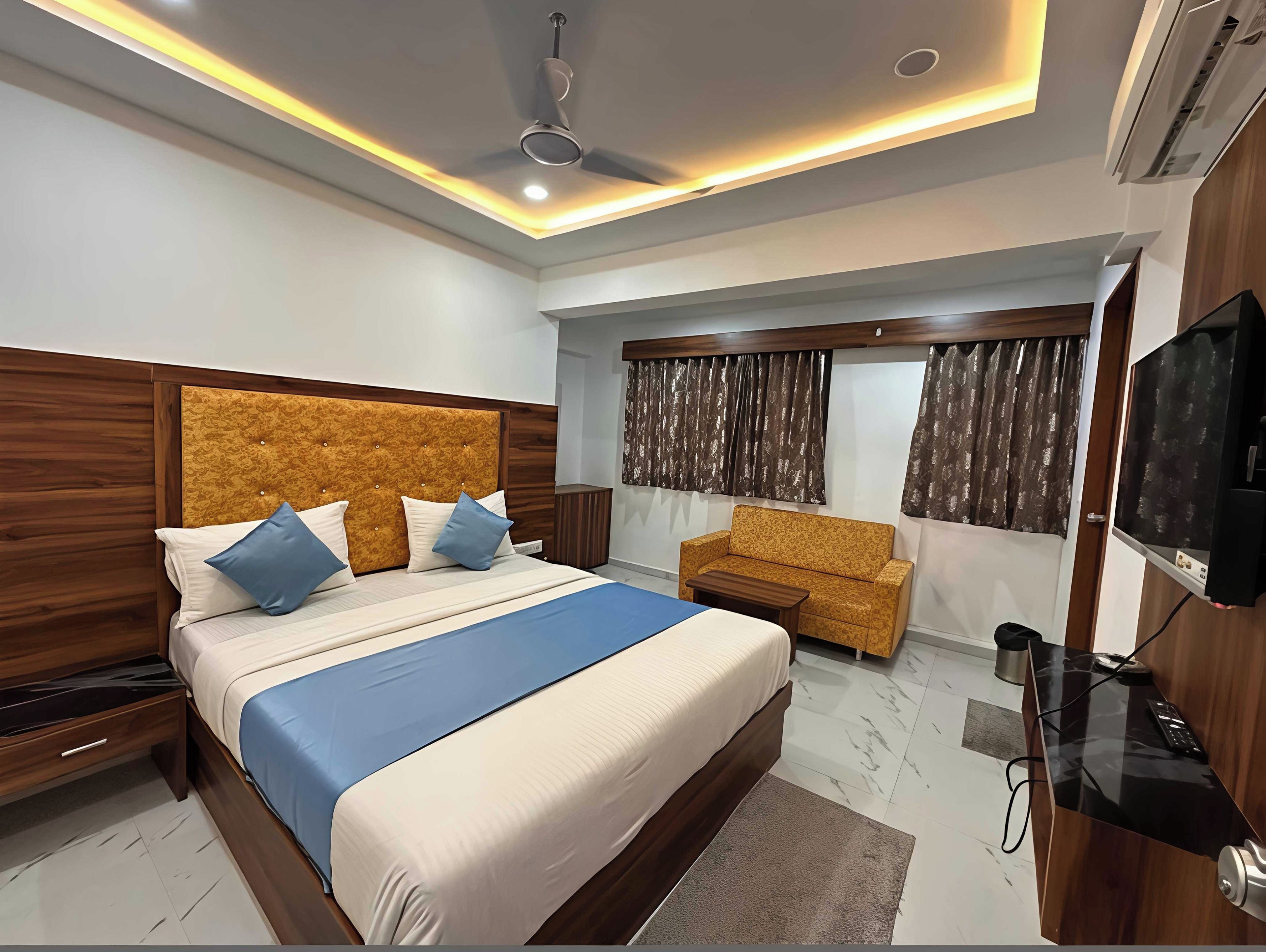 A modern hotel room with a large bed, a sofa, a TV, and a ceiling fan.