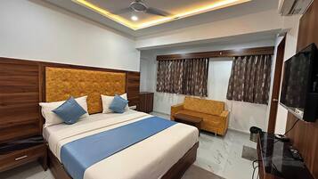 A modern hotel room with a large bed, a sofa, a TV, and a ceiling fan.