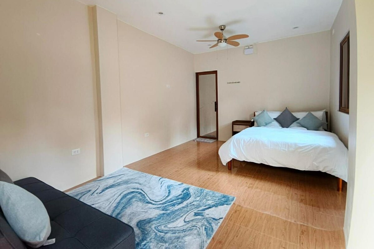 A bedroom with a bed, a ceiling fan, a wooden floor, and a door leading to another room.