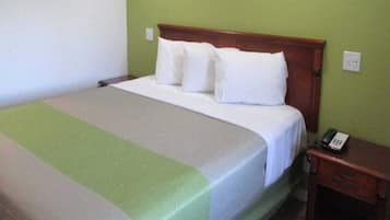 Een enkel bed met een houten hoofdeinde, een groen-witte spreideken en een nachtkastje met een telefoon.