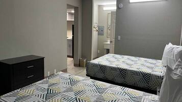 A bedroom with two beds, a dresser, and a bathroom visible in the background.