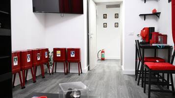 Un soggiorno moderno con una televisione a schermo piatto, bidoni della spazzatura rossi, un estintore e un divano rosso.