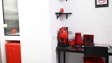 Ein kleines Zimmer mit einem schwarzen Tisch, einer roten Kaffeemaschine und einem roten Stuhl.