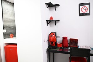 A compact room with a black table, a red coffee machine, and a red chair. - Siren Lot (Naples)