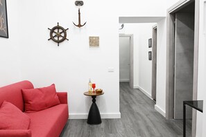 A modern living room with a red sofa, a small round table with a bottle and glass, and a hallway leading to a door. - Siren Lot (Naples)