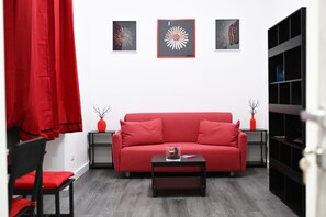 A red sofa, a black coffee table, and a red chair in a room with a white wall and grey flooring. - Siren Lot (Naples)