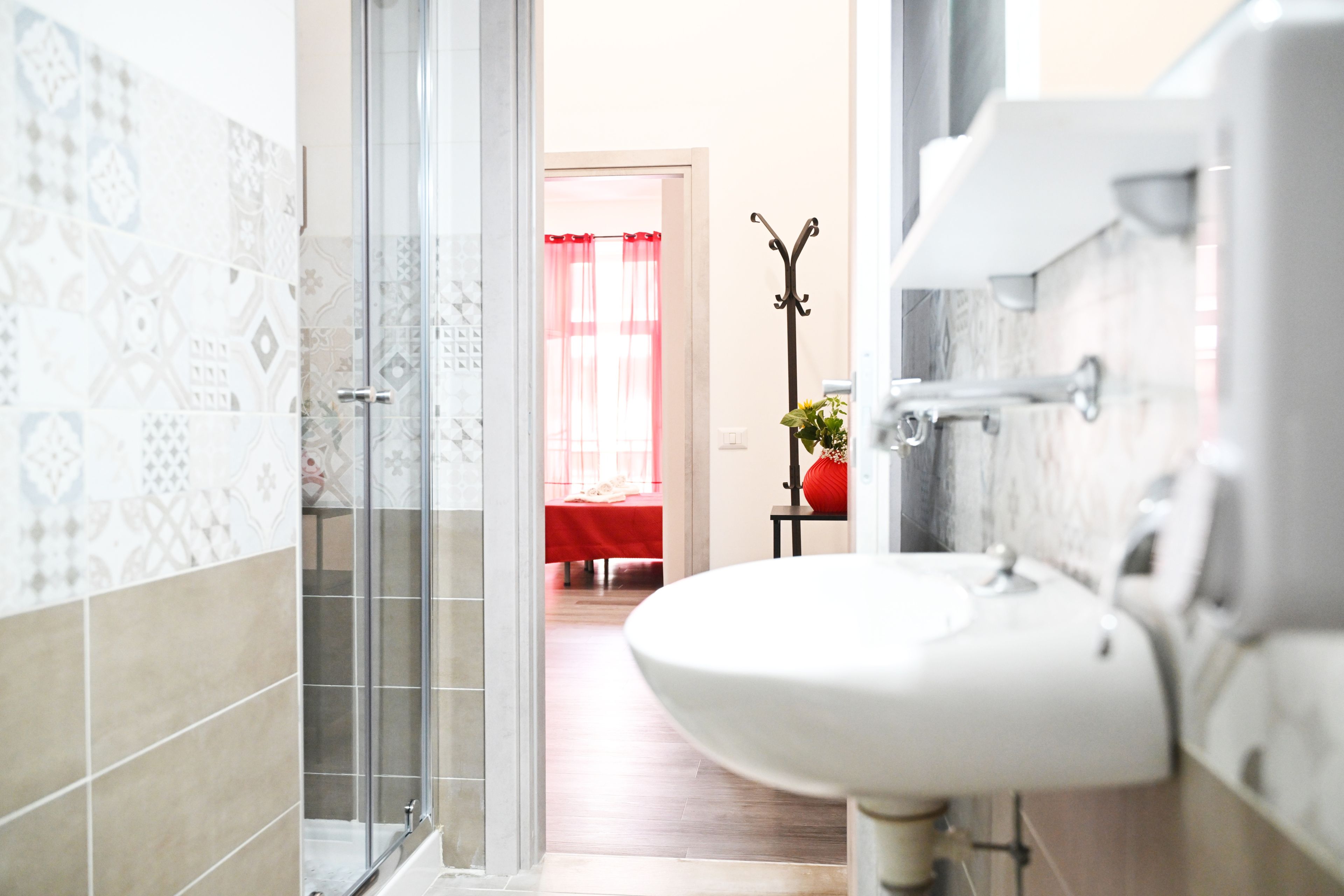 Un bagno con un lavandino bianco, box doccia in vetro e piastrelle decorate.